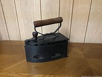 Vintage cast-iron iron with scalloped lid and wooden handle, shown closed on wooden surface.