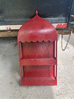 Front view of red decorative wall-mount shelf showing two open shelves with diamond pattern back and pointed dome top.