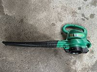 Photo of the full electric leaf blower showing its long black nozzle and green casing on concrete surface.
