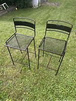Front view of two metal mesh outdoor bar chairs on grass, showing seat and frame details.