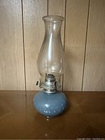 Front view of the oil lantern showing blue hobnail glass base and clear chimney with metal burner.