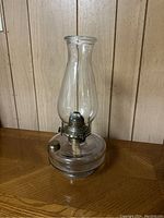 Clear glass oil lantern centered on a wooden surface with a wood panel background.
