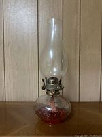 Front view of oil lantern showing clear glass base with red liquid, metal burner, and clear glass chimney