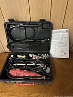 Open plastic case showing red rotary tool, flex shaft, assorted accessories, and instruction manual inside.