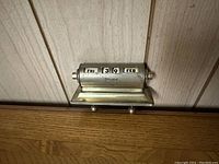 Metal day tracker with numbers and month visible, silver-tone with semi-cylindrical rotating parts.