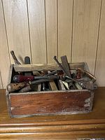 Wooden toolbox with various hand tools inside including scrapers and files with wooden handles