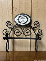 Front view of black metal toilet paper roll holder with decorative scrollwork and 'Salle de Bain' plaque.