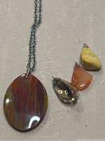 Photo showing three small natural stone pendants and one large oval pendant on chain, on a light surface.