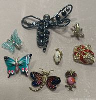 Image of seven vintage brooches including butterflies, dragonfly, frog, owl and a gift box design on a wooden surface.