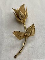 Gold tone metal rose brooch with detailed textured petals and leaves photographed from an angle showing the curled rose petals and detailed leaves.