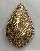 Front view of a gold tone large teardrop brooch with textured abstract linear design and twisted rope edge