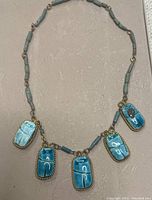 Full view of the necklace showing the arrangement of faience beads and scarab pendants against a neutral background.
