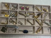 Tray with various vintage men's cufflinks and tie clips in gold-tone and silver-tone metal finishes, displaying a range of geometric, smooth, and adorned designs.