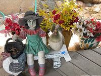 Garden ceramic figure of a girl and rooster next to colorful faux flowers in vases