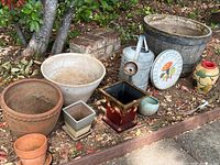 Full view of all items in lot arranged on ground including pots, watering can, and thermometer