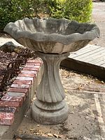 Full view of the assembled bird bath showing the fluted pedestal base and scalloped basin with some weathering and moss.