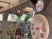 View showing large outdoor thermometer, smaller thermometer above it, and three wind chimes with stained glass dangler