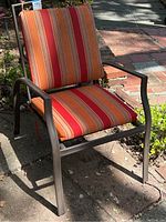 Outdoor metal patio chair with reclining back and striped cushion showing wear, soil, and weathering.