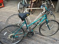 Peugeot road bicycle showing teal and white frame, black saddle, drivetrain and tires on wooden floor.