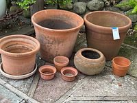All eight terra cotta pots arranged outdoors on stone and wood deck; visible variety in sizes and shapes with natural weathering and no cracks.