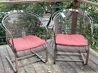 Front view of two metal patio chairs with red cushions on a wooden deck.