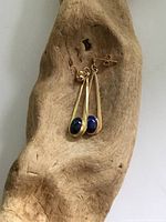 Two vintage 14K yellow gold earrings each set with oval Lapis Lazuli stones, displayed on a wooden base against white background.