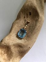 Top view of the blue topaz pendant on a wooden prop showing the front view with gemstone and gold setting.