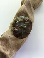 Top side of antique carved jade pendant showing floral botanical carving in green and brown tones.