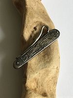 Close-up of the engraved decorative metal body of the sewing hook lying on a wooden surface, showing tarnish and wear.