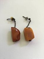 Front view of antique raw Baltic amber dangle earrings showing amber pieces attached to white metal chain links and posts on white background.