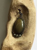 Front view of antique silver teardrop pendant featuring an oval agate stone with silver bead accents, placed against a wooden background for texture contrast.