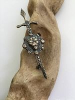 Front and angled view of antique silver lion and sword brooch showing detailed lion's head in center and sword extending vertically.