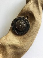 Front view of antique sterling silver pin showing embossed figure and detailed border.