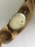 Front view of oval silver locket showing smooth surface with small floral engraving.
