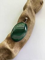 Front view of large oval green malachite pendant set in silver on a wooden textured surface.