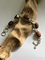 Full view of the silver tone goldstone panel bracelet laid on a piece of textured wood showing the bracelet shape and details.