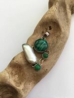 Sterling silver pendant placed on a wooden textured background showing the front with malachite, pearl and jade stones.