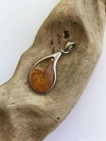 Front side view of the teardrop Baltic amber pendant resting on a wooden background, showing amber's amber-orange hues and silver bezel.