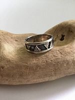 Sterling silver band ring with triangular geometric pattern resting on a wooden surface, showing tarnish and surface wear.
