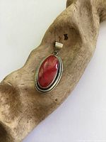 Front view of oval red coral pendant set in detailed sterling silver bezel with rope edge