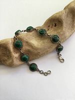 Full view of vintage sterling silver bracelet with eight oval malachite stones, laid on wooden surface.