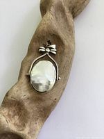 Front side of pendant showing polished mother of pearl stone in sterling silver setting, with bow detail at top