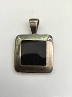 Front view of chunky square sterling silver pendant with inset black onyx stone on white background.