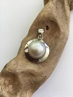 Front view of sterling silver pearl pendant resting on rustic wood background showing the polished silver frame and prominent dome-shaped pearl.
