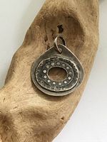Front view of vintage sterling silver pendant with raised oval center and circular indentations on natural wood background.