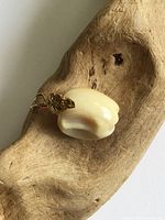 Close-up side view of the apple pendant showing the carved natural material and gold tone metal stem and leaf attached with a loop for chain.