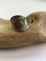 Wide sterling silver ring showing front cutout floral design and minor tarnish resting on wood surface.