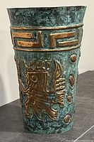 Angled left side view of copper can showing a Mayan/Aztec figure in raised copper detail on patinaed surface.