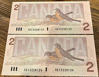 Reverse side of two consecutive Canadian $2 bills dated 1986 featuring American robin birds and large 'CANADA' text with serial numbers.
