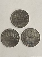 Reverse side of three 1986 Canadian coins showing Voyageur design with canoe and voyageurs.